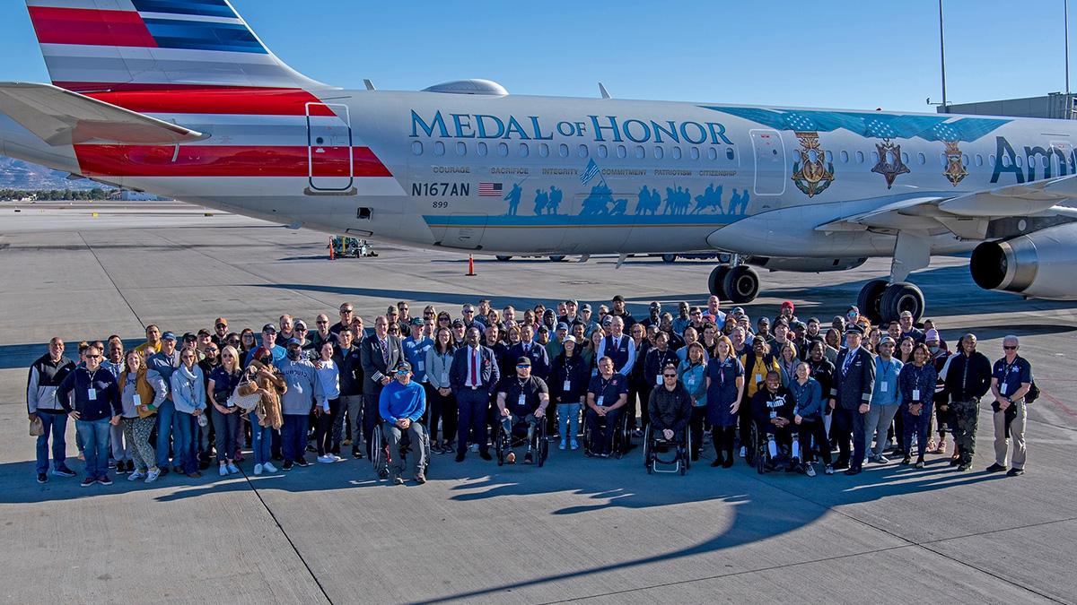 A large group collected together on a tarmac in front of an airplane