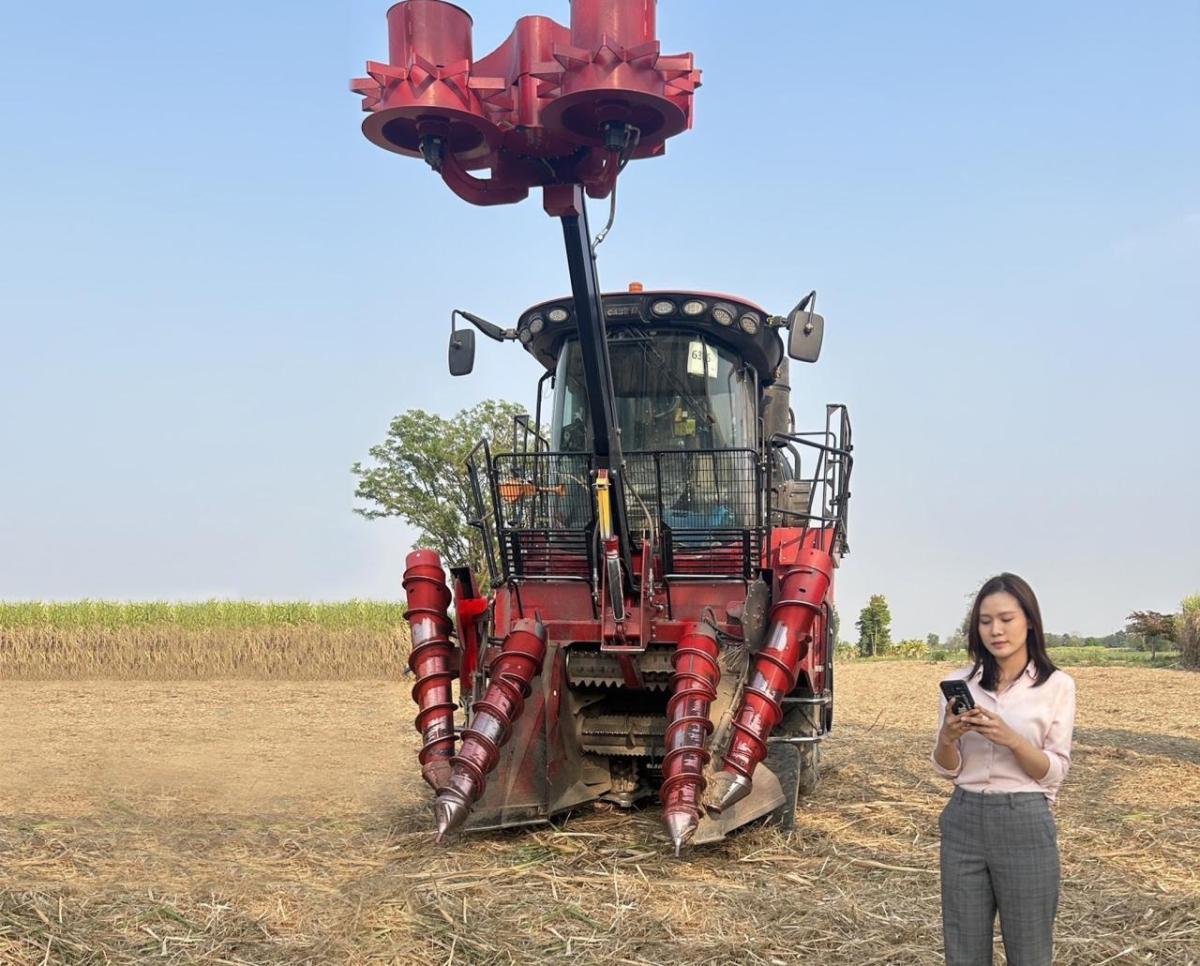 A red piece of agricultural equipment in a crop field, with a person stood to the right 