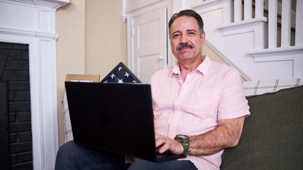 A person in a couch using a laptop. A folded american flag behind them.