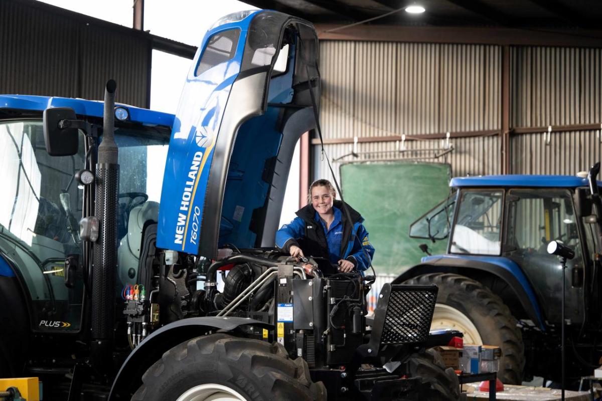 A mechanic standing next to a farm tractor with an open hood.
