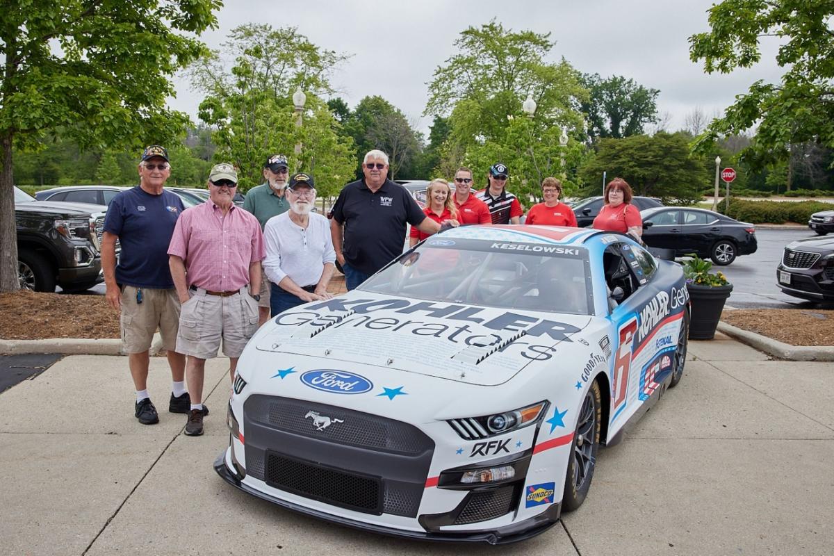 a group of people stand behind a race car, some wearing military service hats