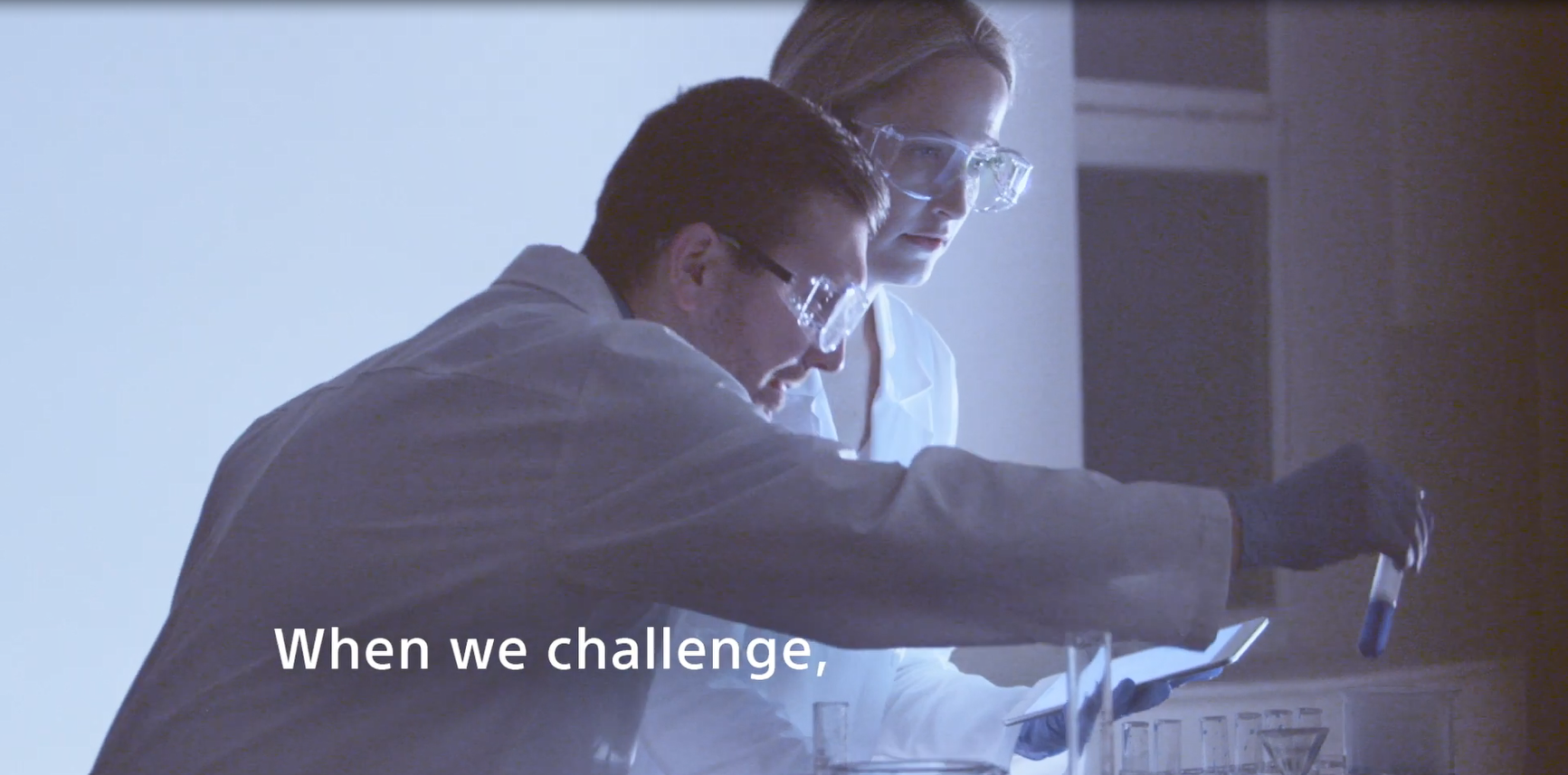 Two people in protective lab goggles, gloves and coats looking over beakers.