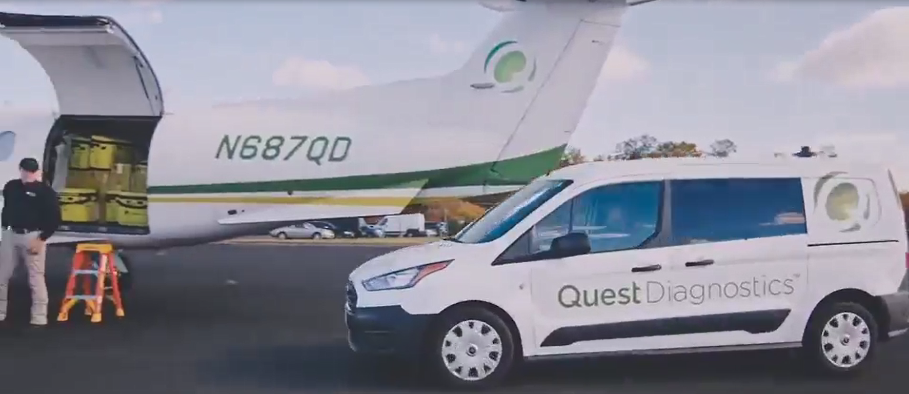 A white car with "Quest Diagnostics" on the side pulls up to a small plane with the same logo.