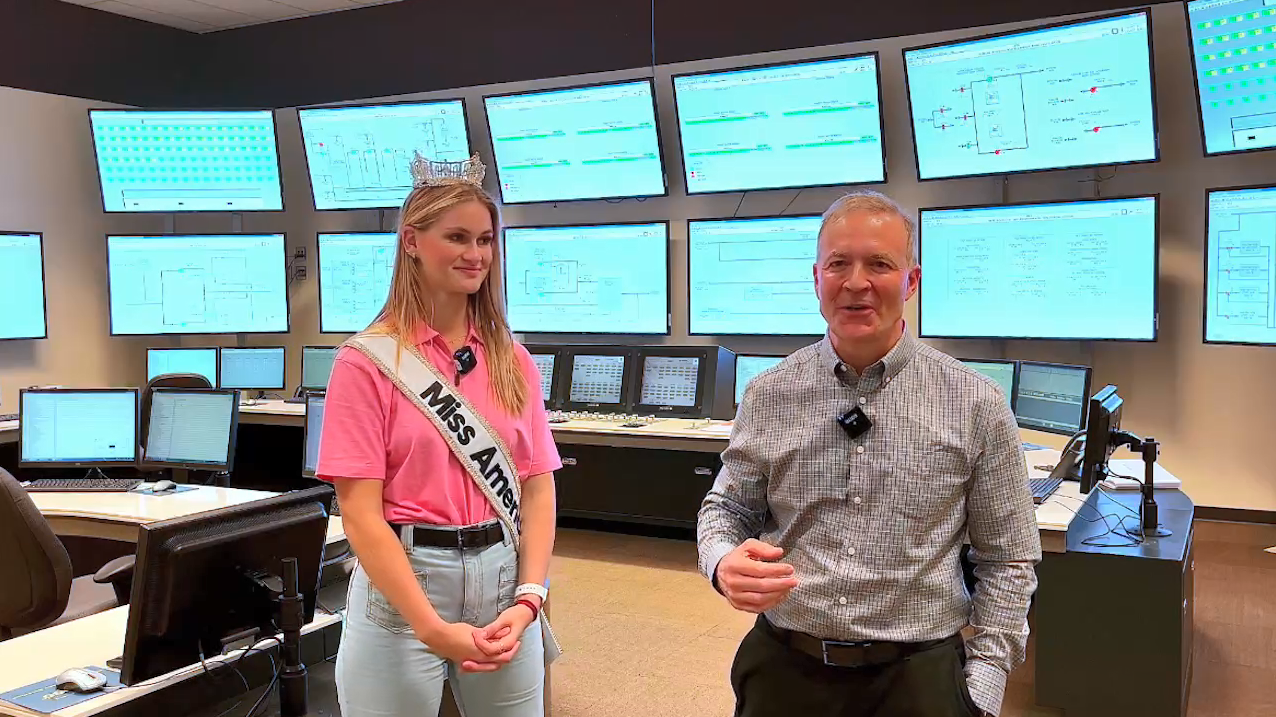 Grace wearing a crown and sash, and a representative from Southern Company in a room full of screens