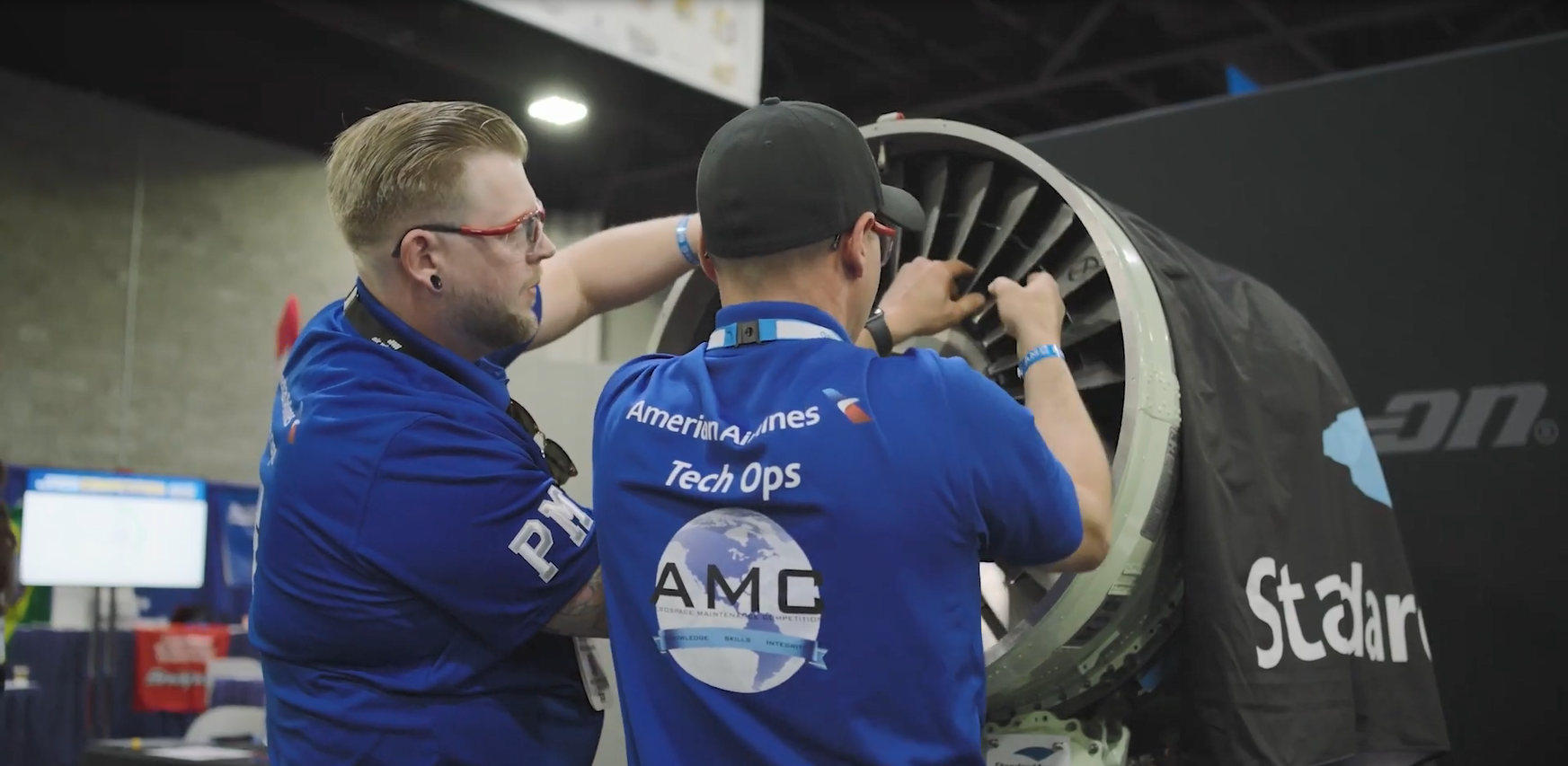 Two people working on an airplane engine, wearing matching shirts with American Airlines logo.