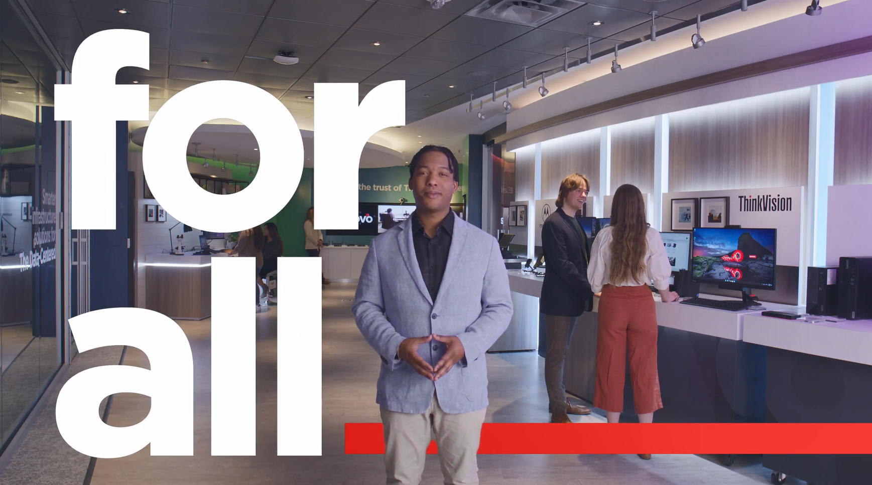 A person standing, talking to the camera, in a product display area. Others behind him talking next to different laptop computers. "for all" imposed on the side.