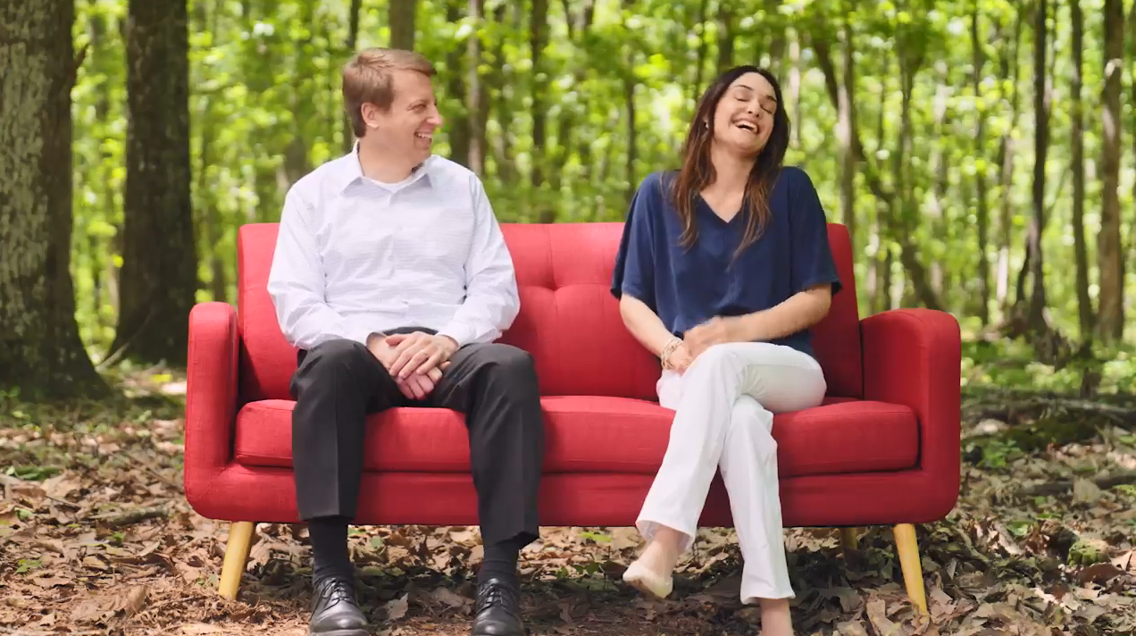 Two people on a red couch in a forested area.