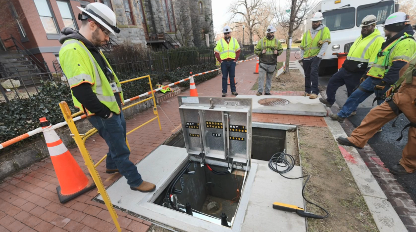 Workers in high-vis clothing and hard hats surround an open hatch in a walkway.