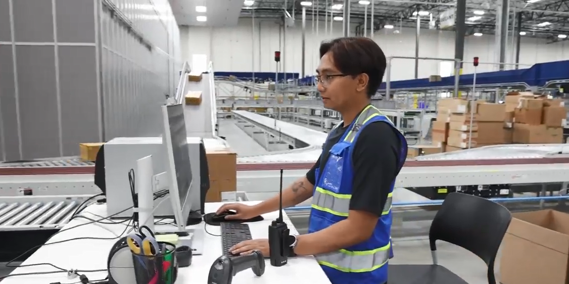 Jerenez Rivera standing at a computer station next to conveyor lines.