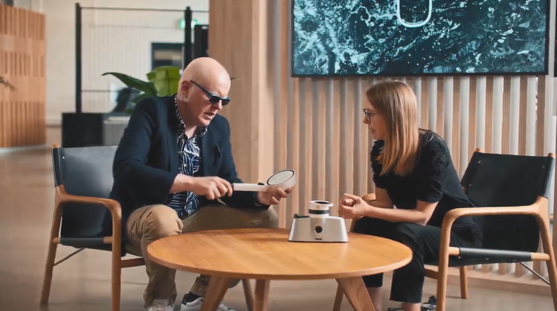 Two people seated at a low table. One holding a shower head.