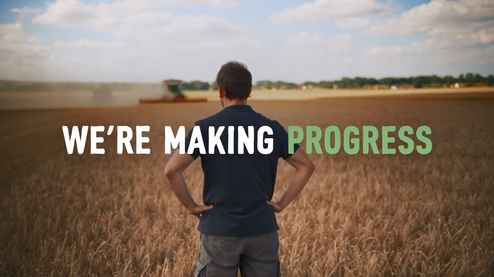 "We're Making Progress" over a person, with hands on hips, looking out over a crop field.