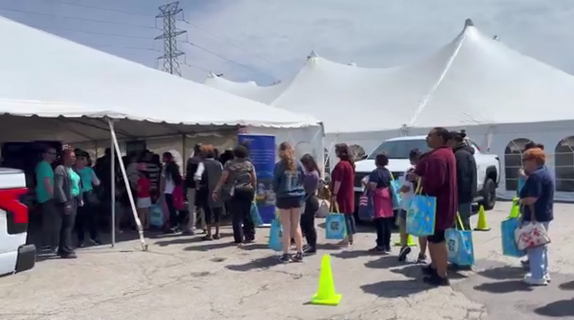 A line of people going under a large white tent. Volunteers standing to the side.