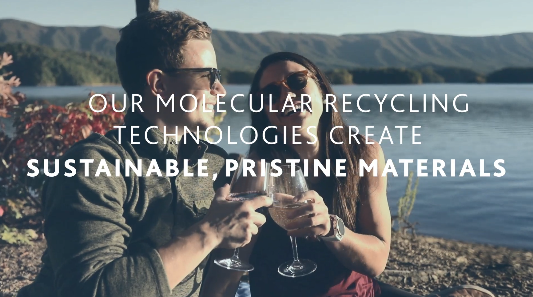 Two people next to a bod of water with drinks, clinking glasses.