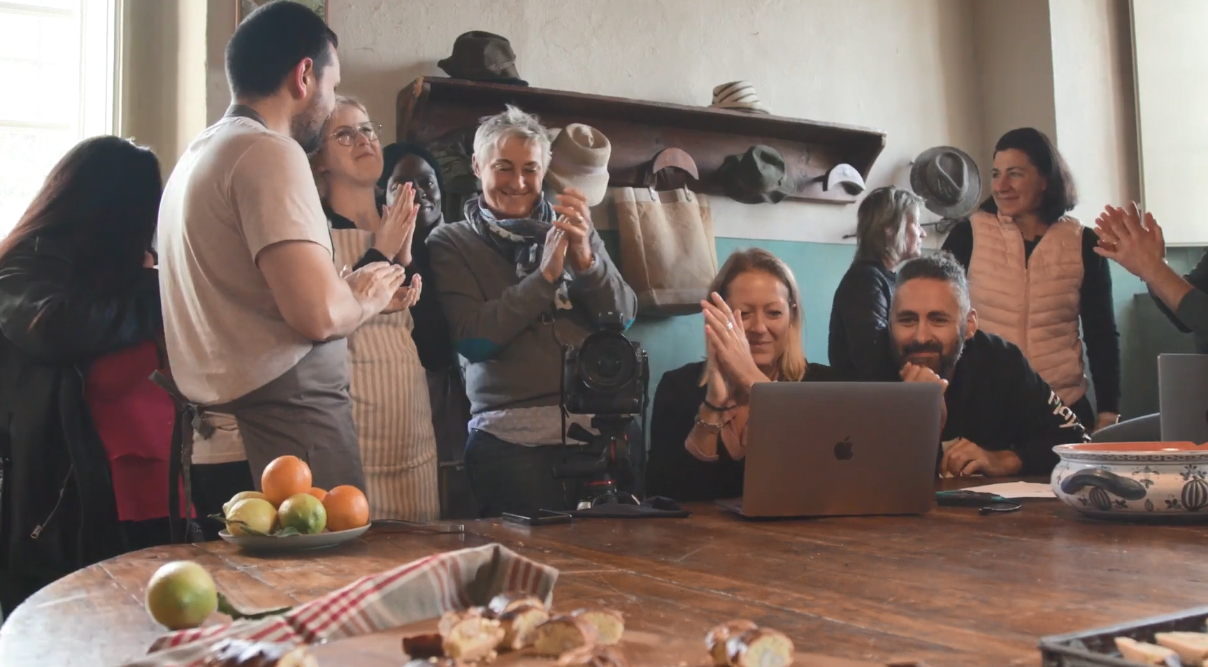 A group of people looking at an open laptop, clapping, in a home setting.
