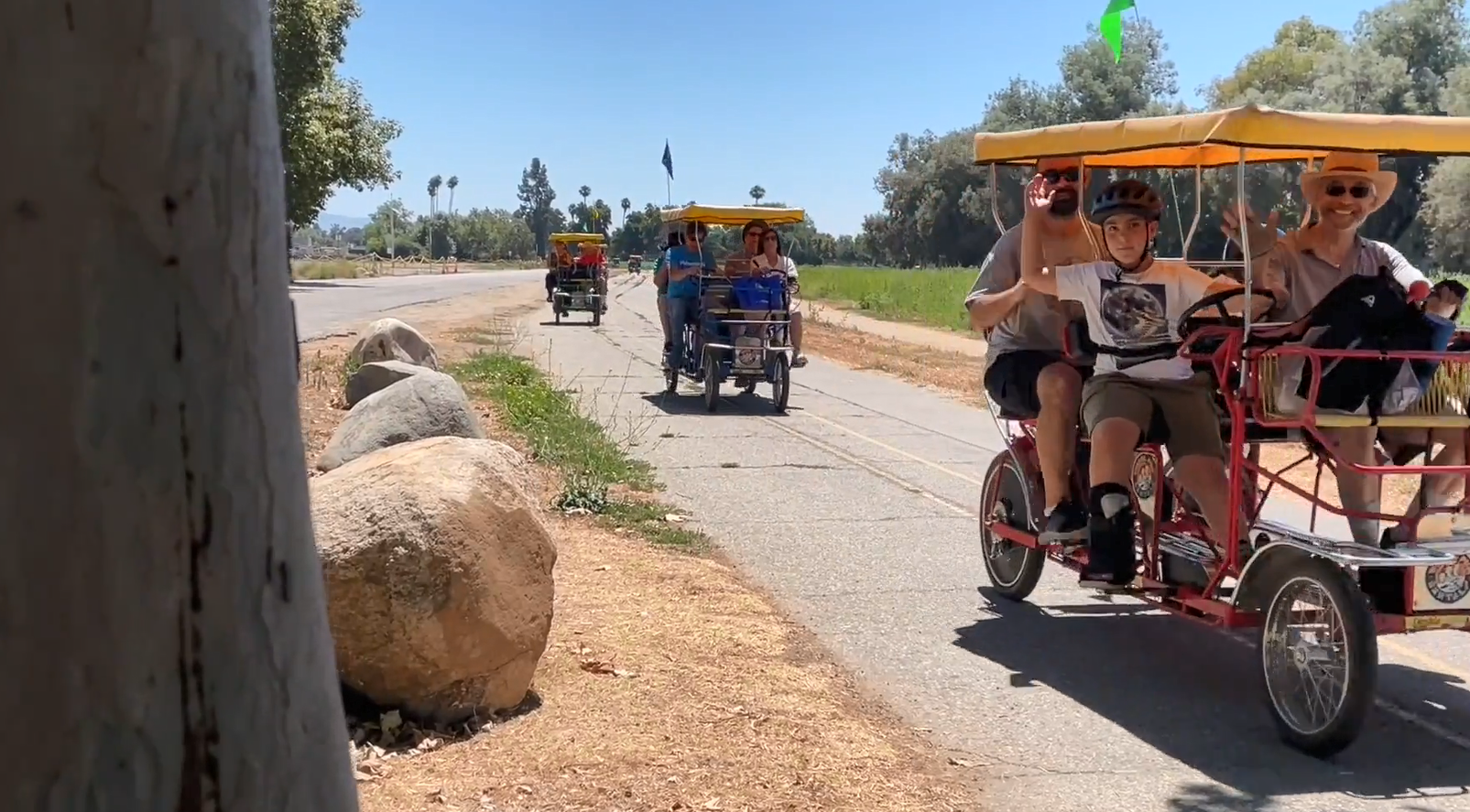 Adults and children riding in covered, pedal-driven carts on a path.
