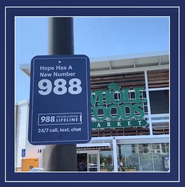 "Hope has a new number 988" sign on a light post outside a "Whole Foods Market"
