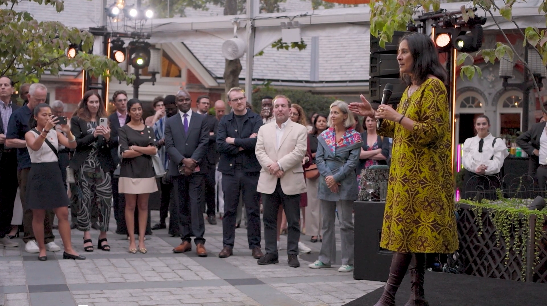 Someone with a microphone, speaking to a small crowd outside
