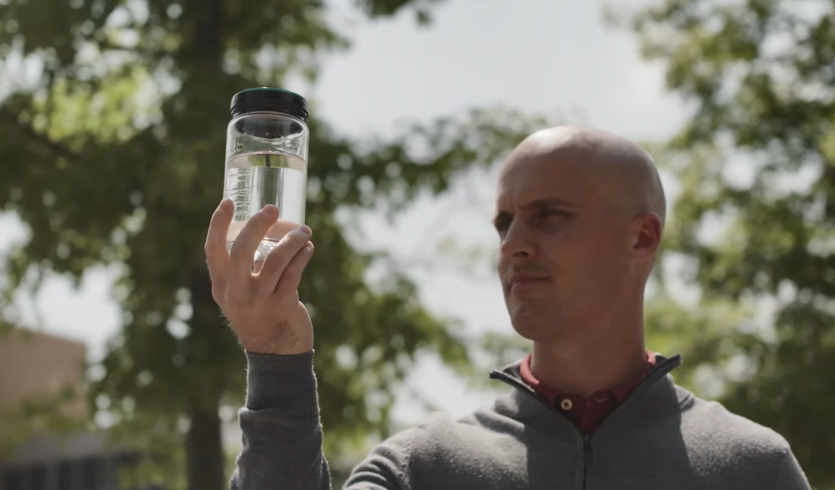 A person holding up a clear bottle of fluid outside.