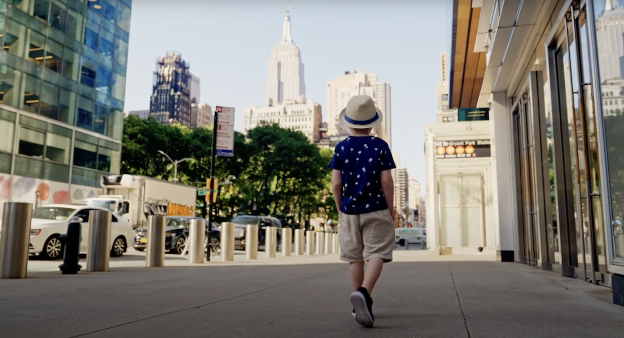 Young boy walking down a street with a hat on.