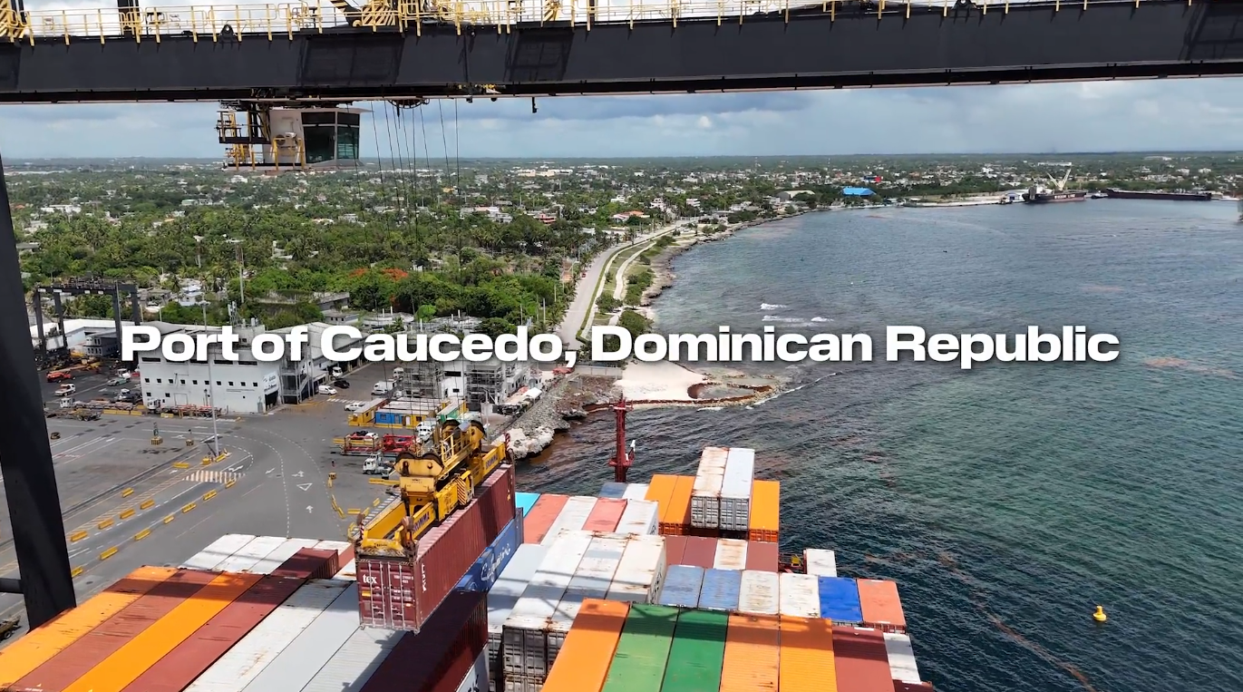 Aerial view of the Port of Caucedo in the Dominican Republic, showing container operations along the coastline with cranes lifting cargo, stacked shipping containers, and the Caribbean Sea in the background.