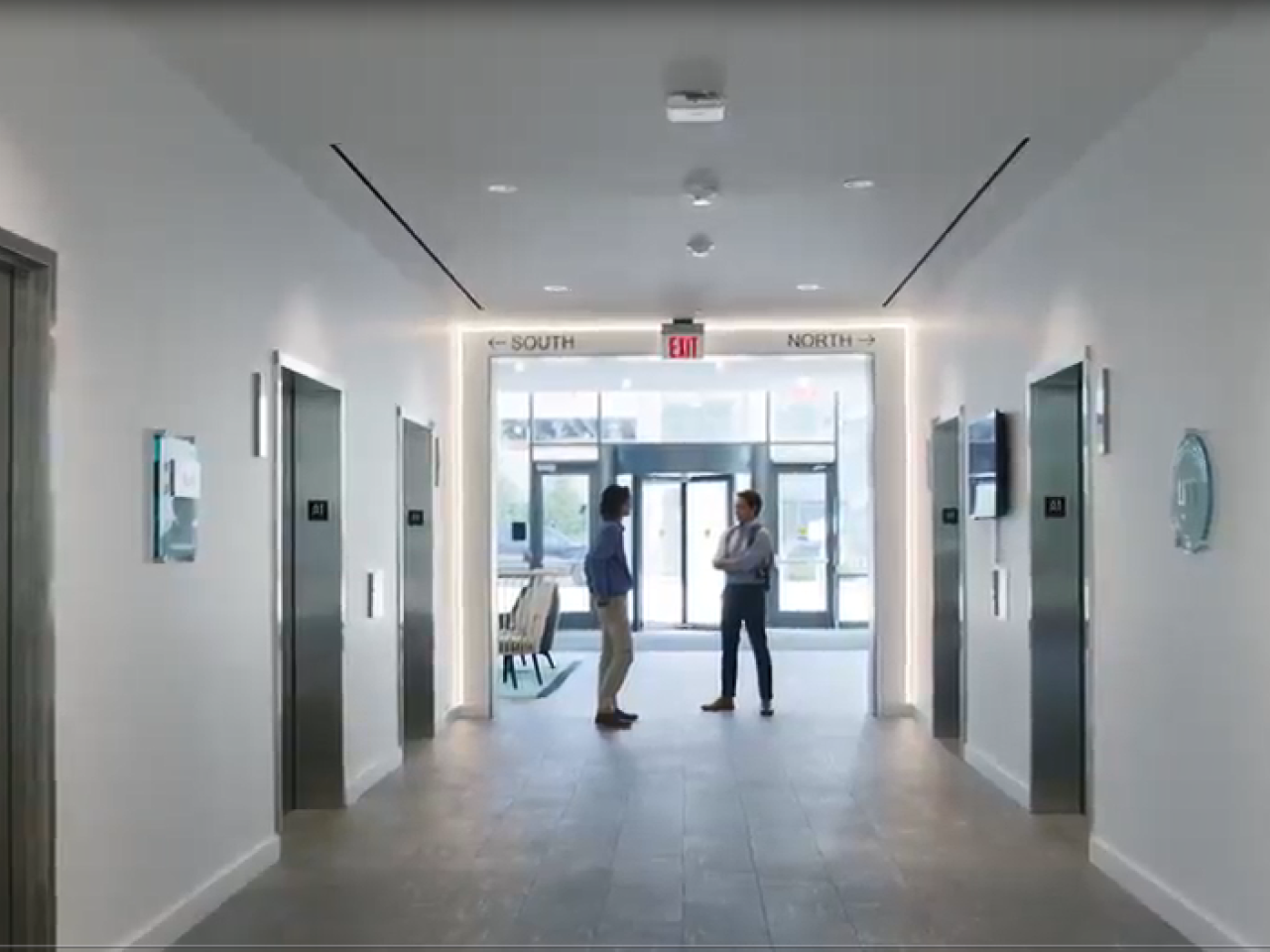 Two people at the end of an office hallway talking with each other.