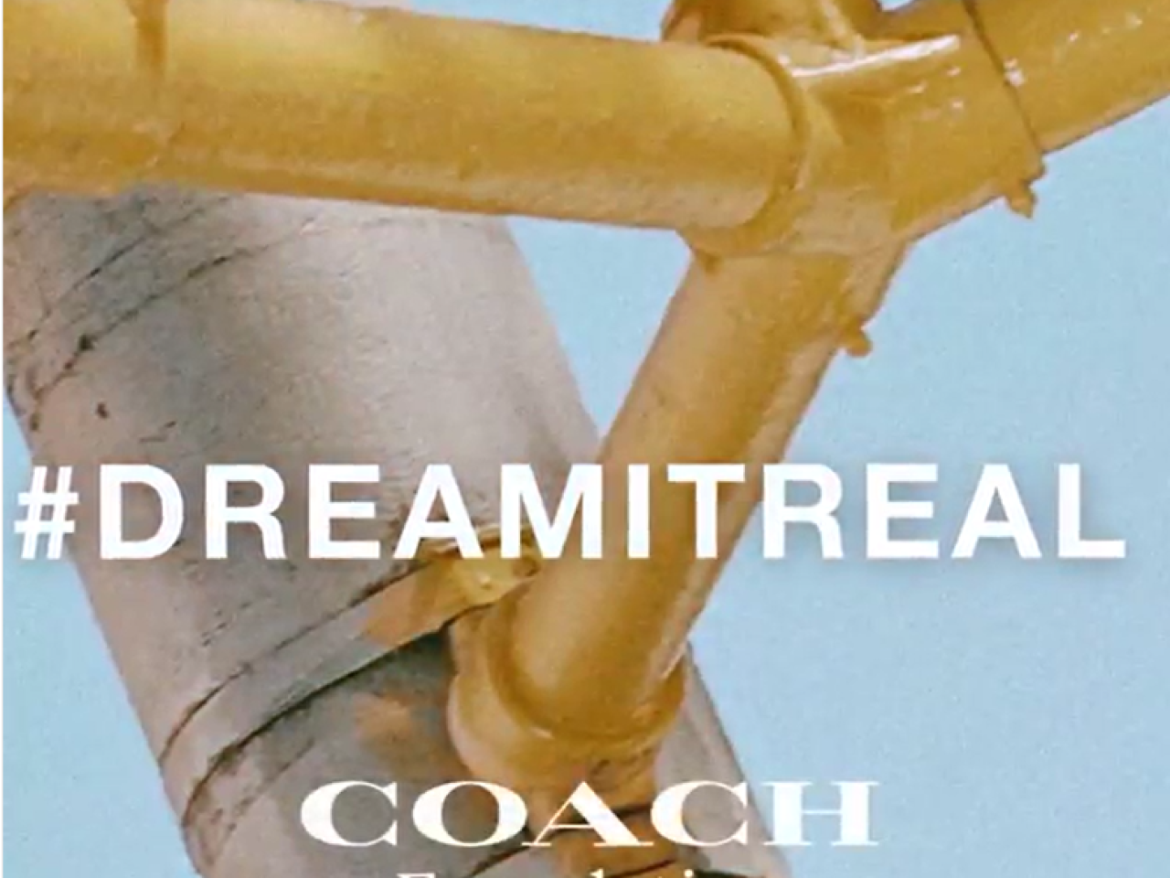 "#DREMITREAL Coach Foundation" gold painted pipes on a light blue background behind the words.