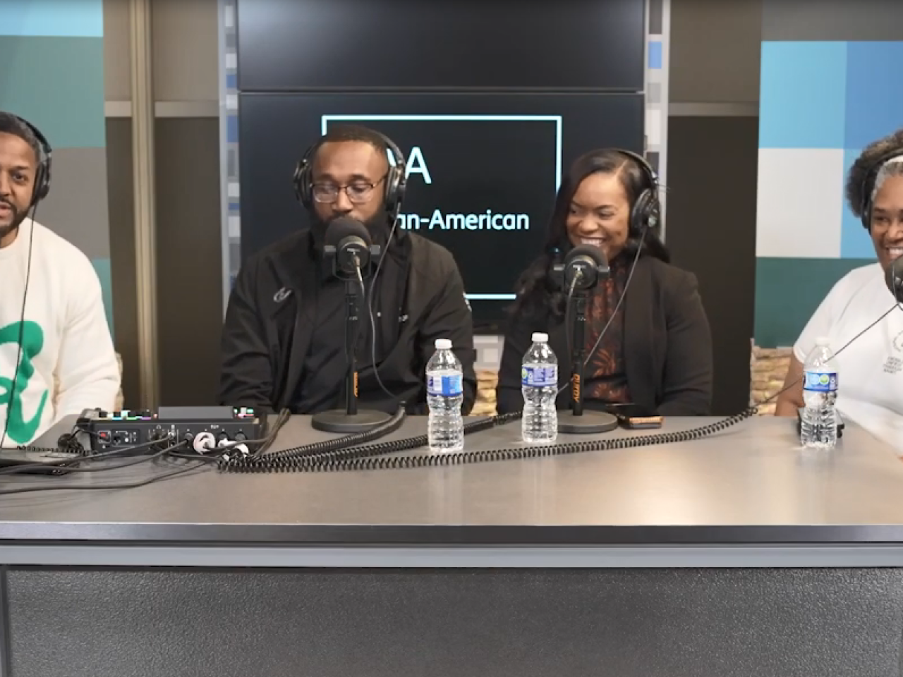 Four people with headsets and microphones, sitting at a desk.