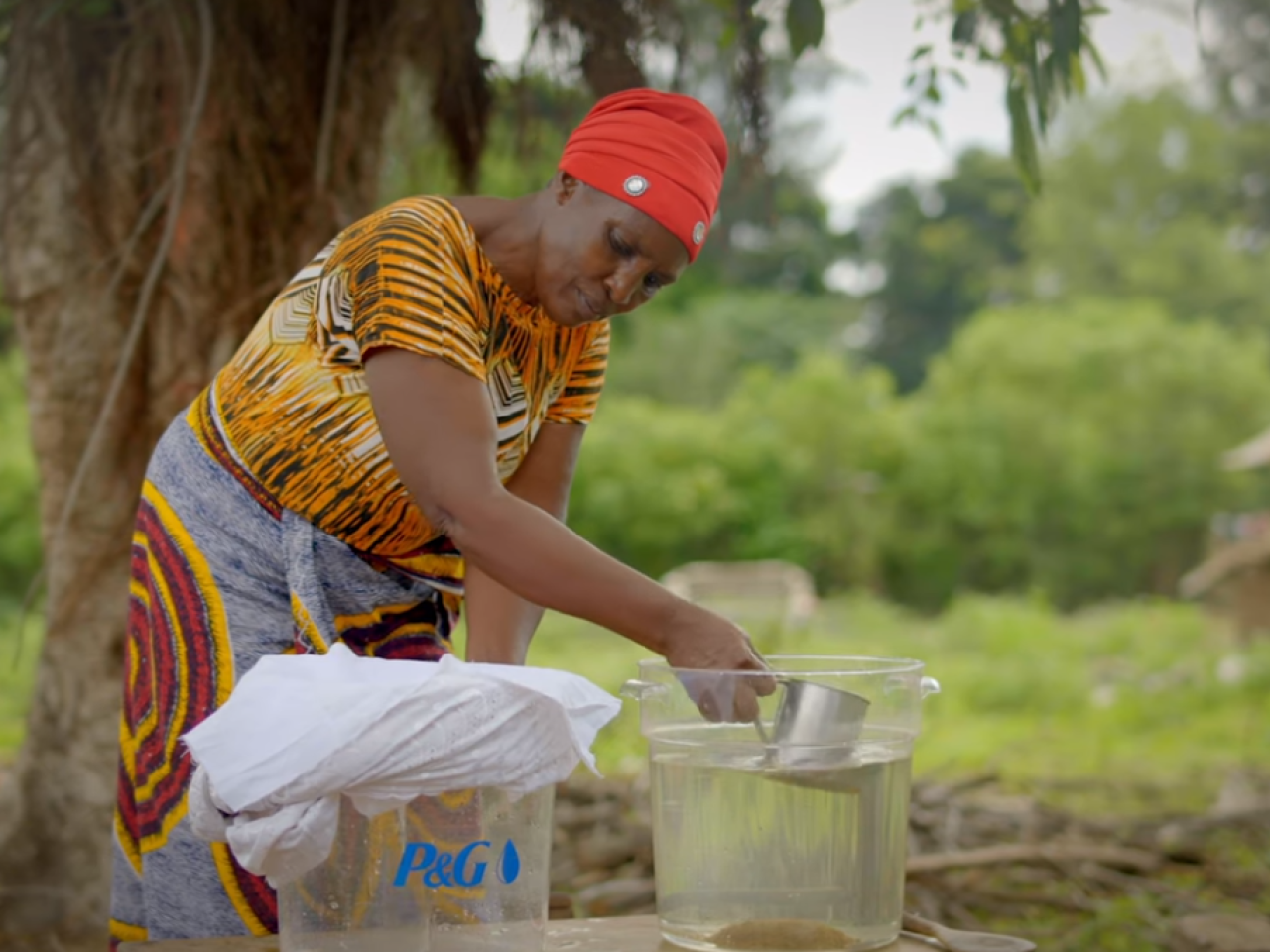 Woman scooping out clean water from a P&G bucket