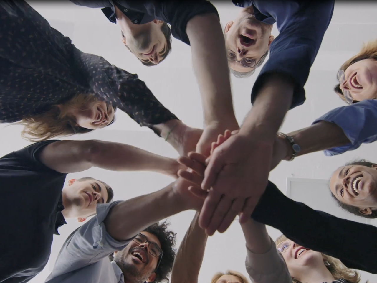 Looking up at a group of people each with a hand in the middle of a circle.