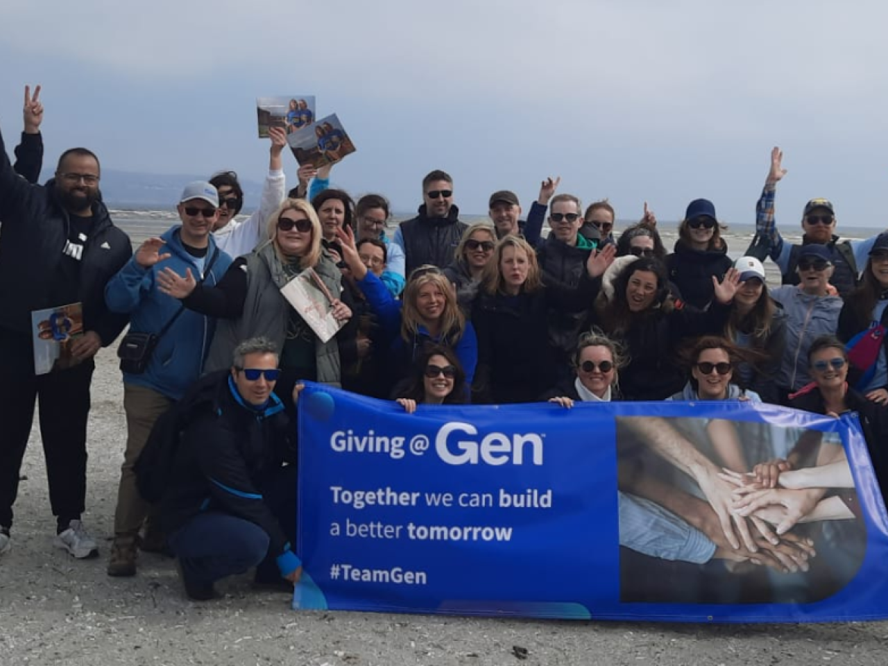 A group of people cheering on a beach, the front row holding a sign "Giving @ Gen".