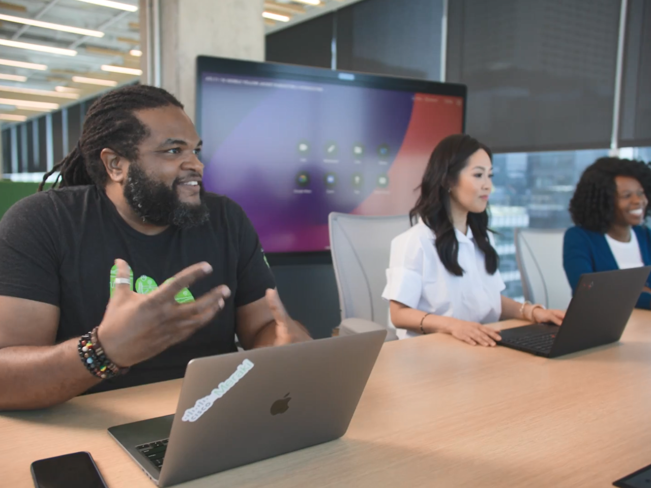 Three people at a long desk. A digital screen behind them.