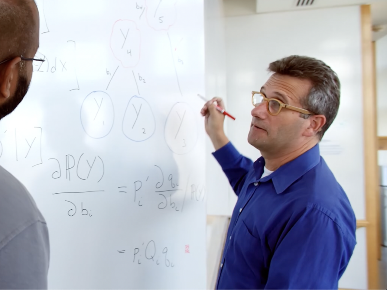 Two people working equations on whiteboard