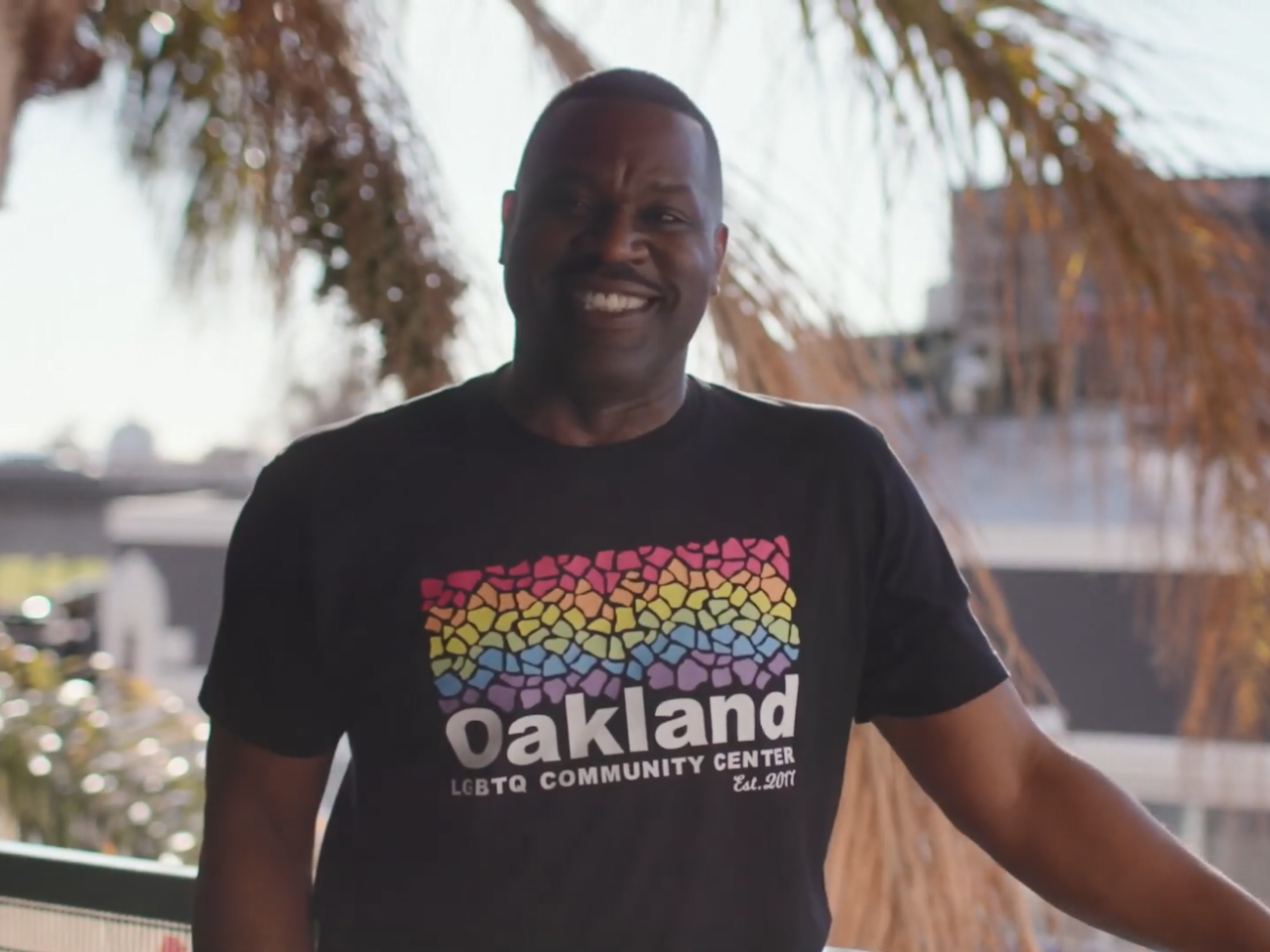 Joe Hawkins standing outside wearing a "Oakland LGBTQ community center" tshirt.