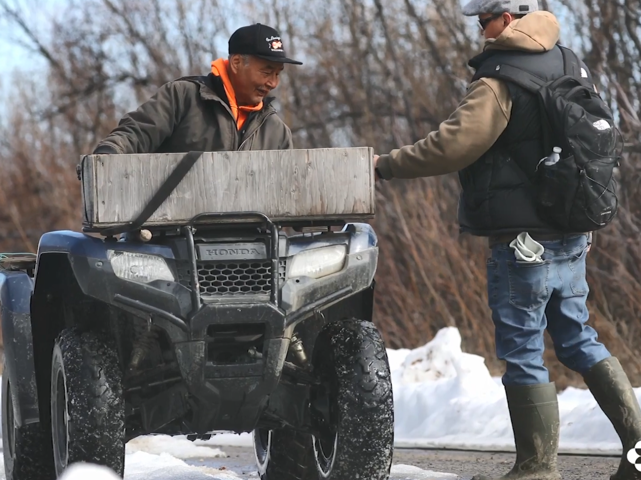A person hand a package to another on an atv.