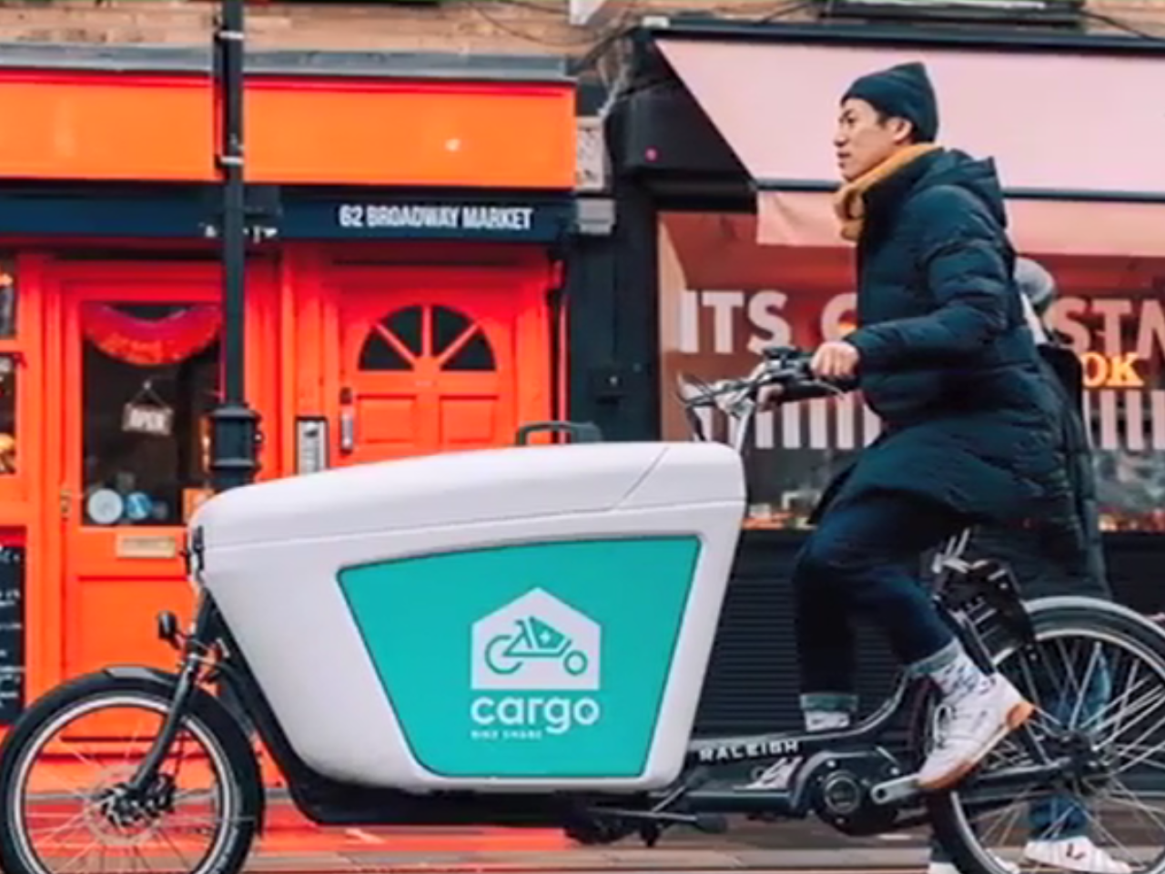 A person on a cargo bike riding past small shops