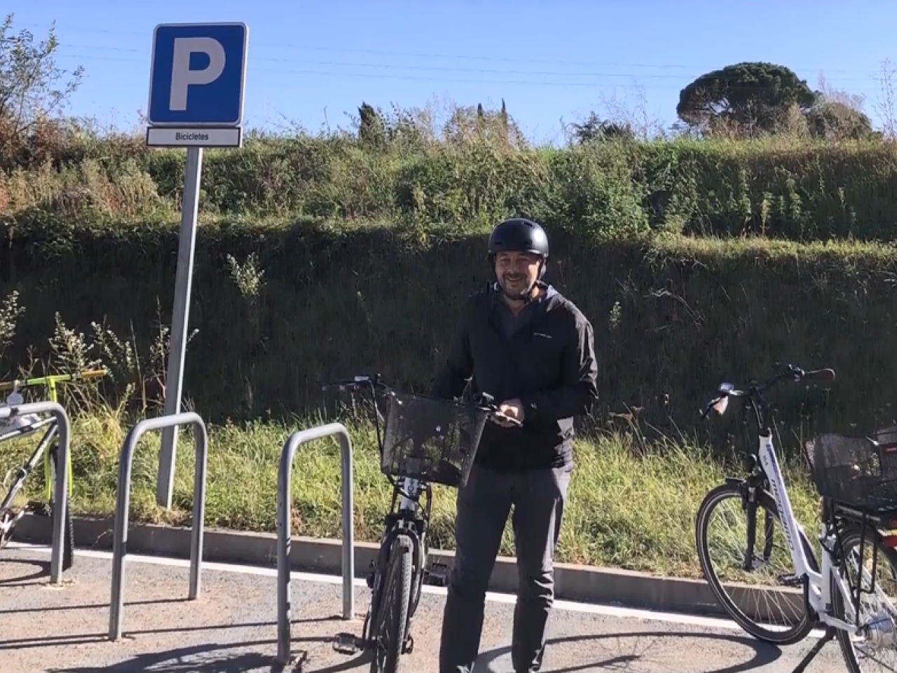 A smiling person standing by a bicycle in a bike parking area.