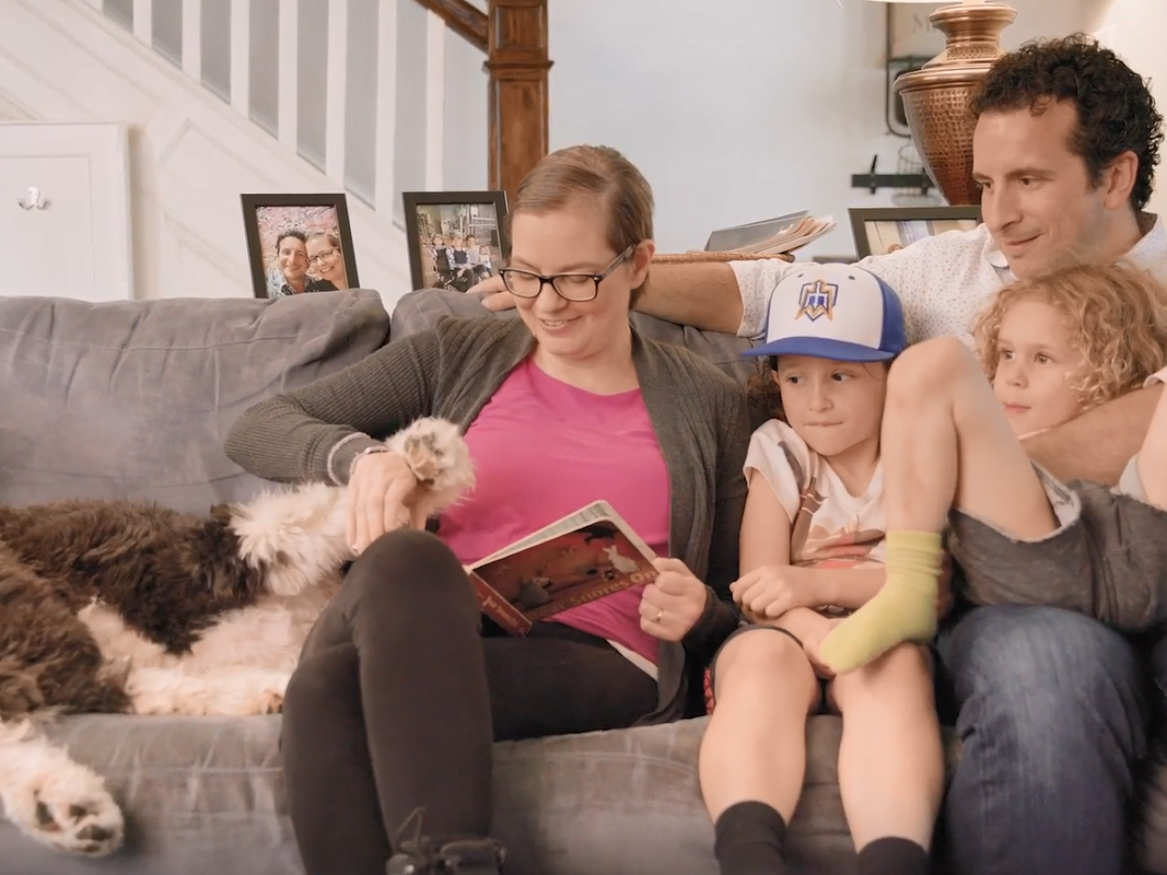 Cara and family seated on a couch reading a book.