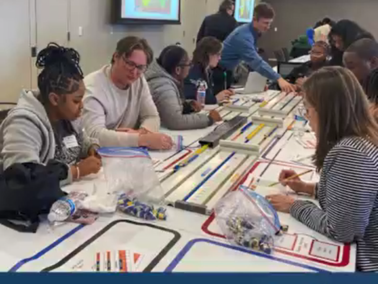 Students and mentors working on a project on a long strip of paper with colored areas.