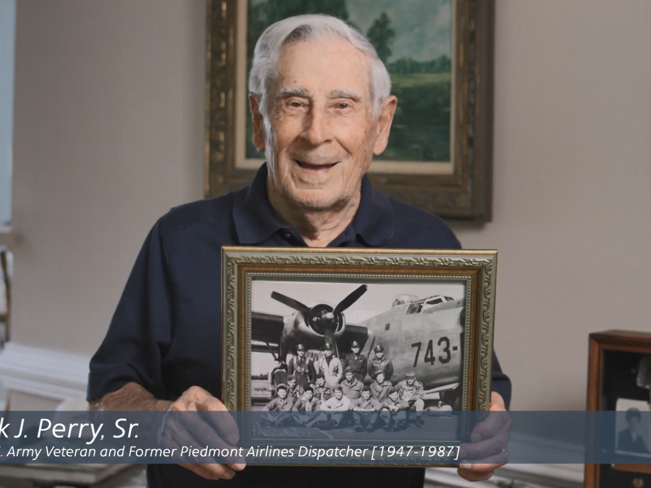 Frank Perry Sr. holding a picture of him and others in uniform by a plane.