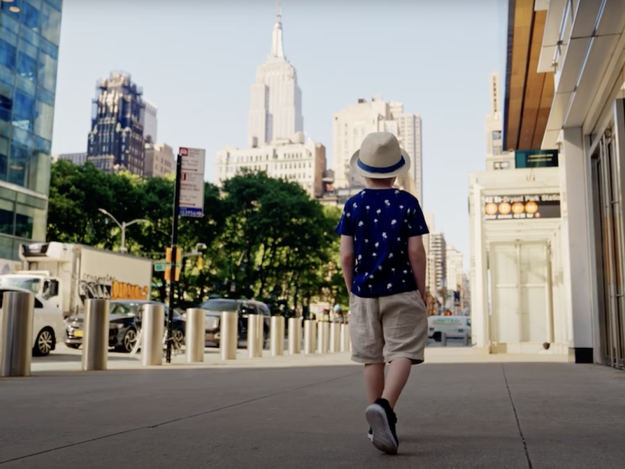 Young boy walking down a street with a hat on.