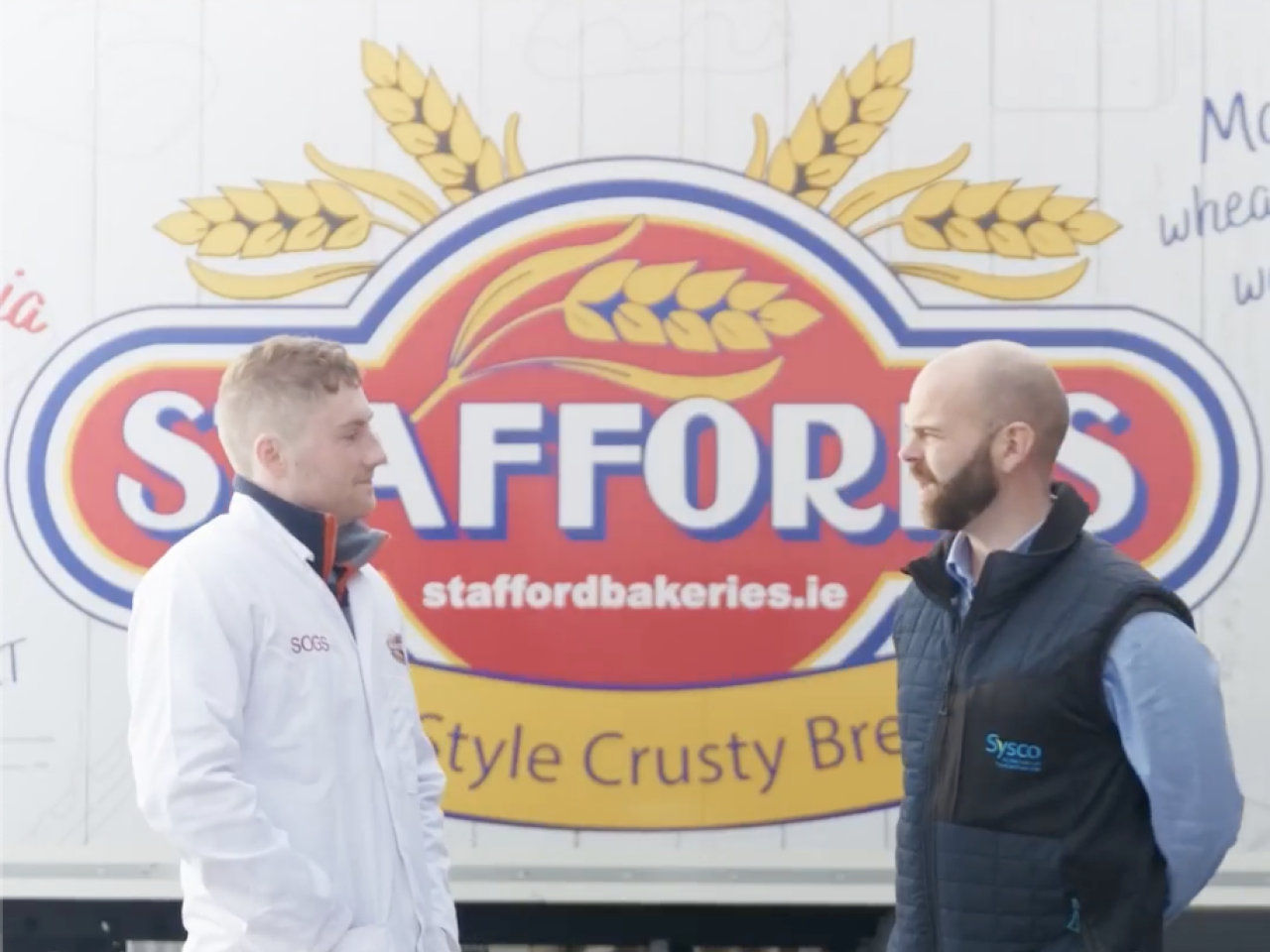 Two people speaking in front of Stafford Bakery truck
