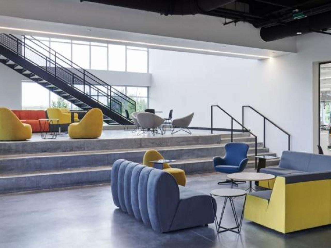 A lobby with blue and yellow seats, which also has a large window looking into a lab