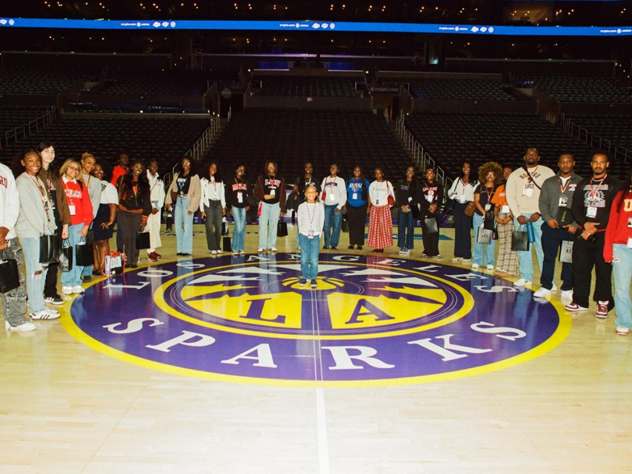 Group of students and professionals standing on the Los Angeles Sparks basketball court for a photo inside Crypto.com Arena.