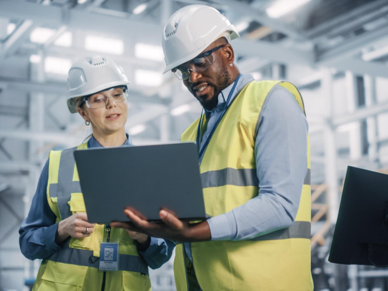 Workers in hard hats and safety vests looking at a laptop