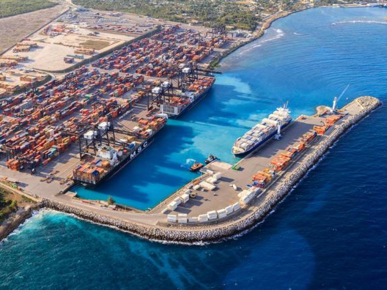 Aerial view of DP World’s Port of Caucedo in the Dominican Republic, showing container ships docked at the terminal, cranes loading cargo, and stacked shipping containers along the turquoise Caribbean coastline.