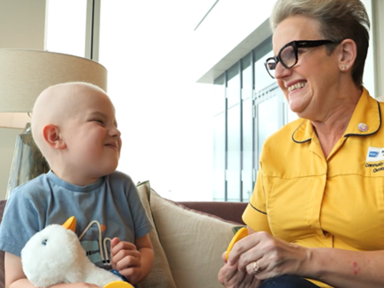 Young cancer patient holding the Aflac Duck and seated with a health professional.