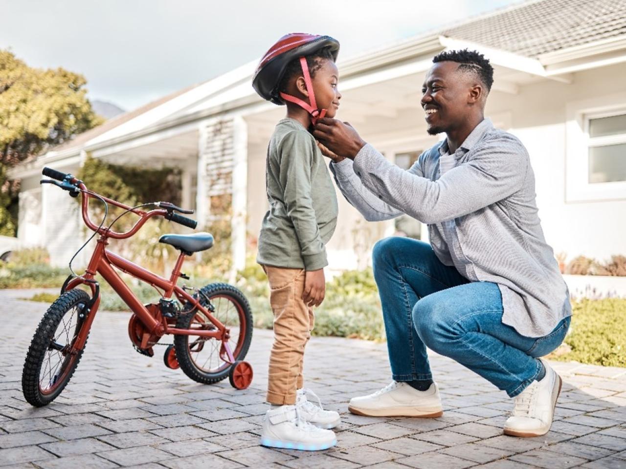 A father helping his son put on his bicycling helmet.