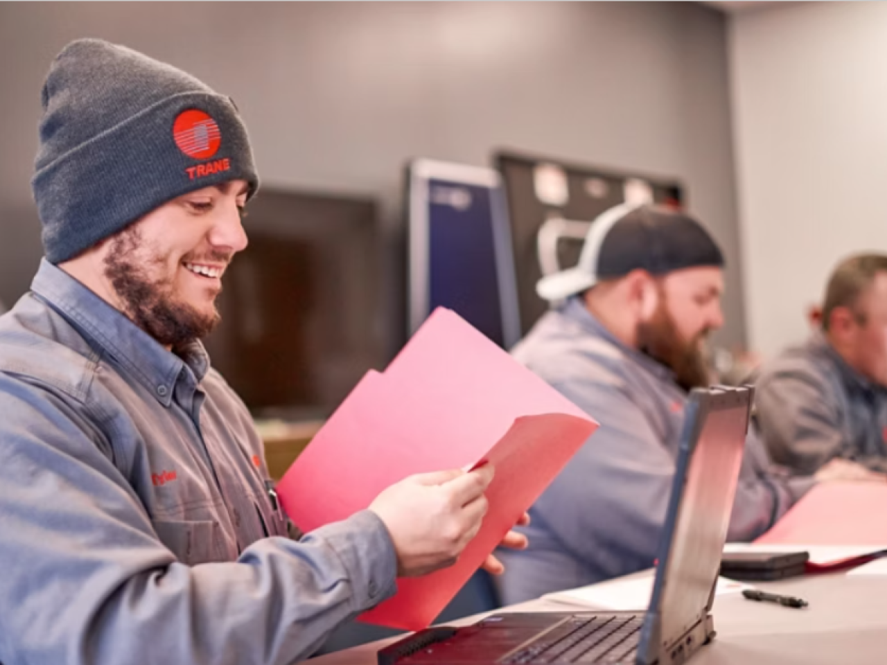 People sitting at a desk with laptops and red folders