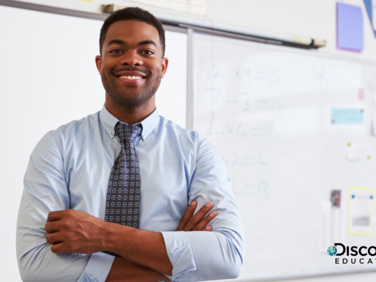 Teacher standing in the front of class with arms crossed, smiling.