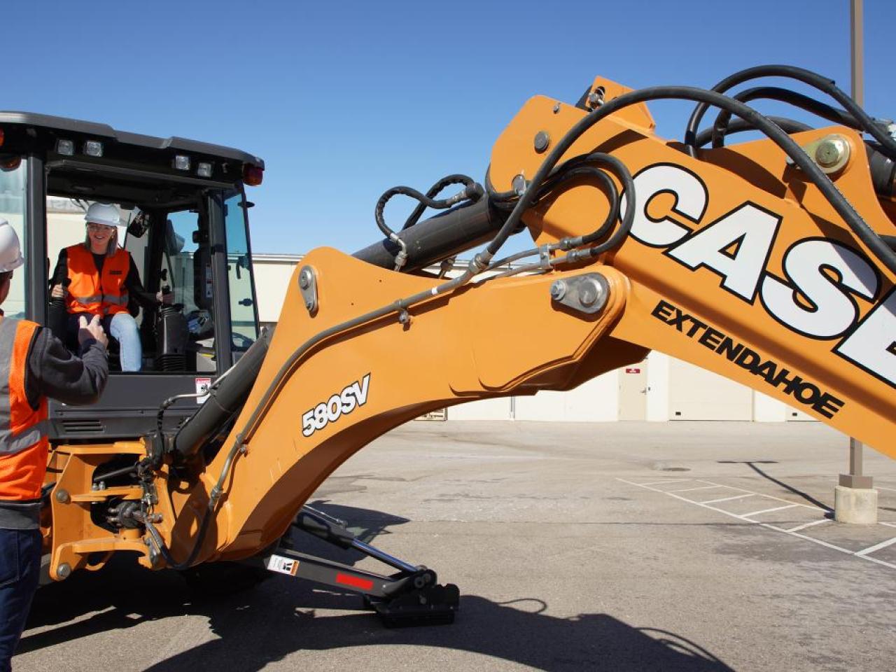 A person operating a large industrial machine, being instructed by a person on the outside.